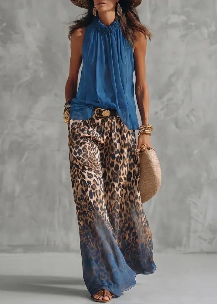 Woman wearing a blue sleeveless top and leopard print pants against a gray background