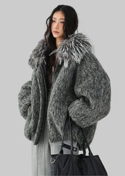A woman wearing a voluminous, oversized fuzzy gray faux-fur jacket with a large shaggy faux-fur collar, styled with a black tote bag against a plain white studio background. 