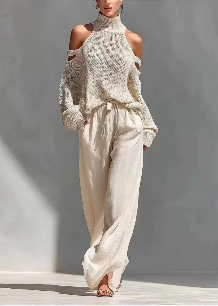 Person wearing a beige knitted top and wide-leg pants against a gray background