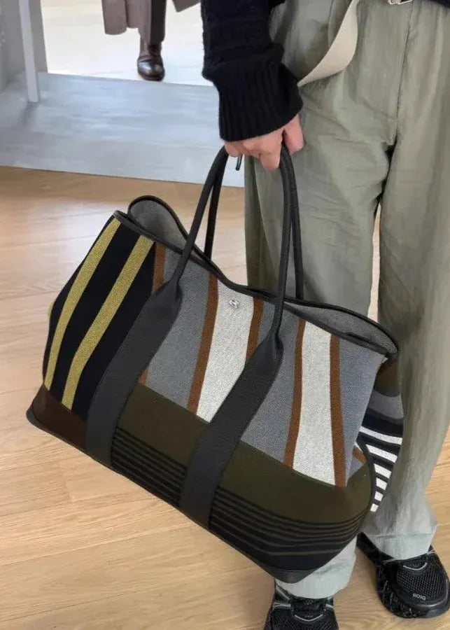 Person holding a striped duffel bag on a wooden floor