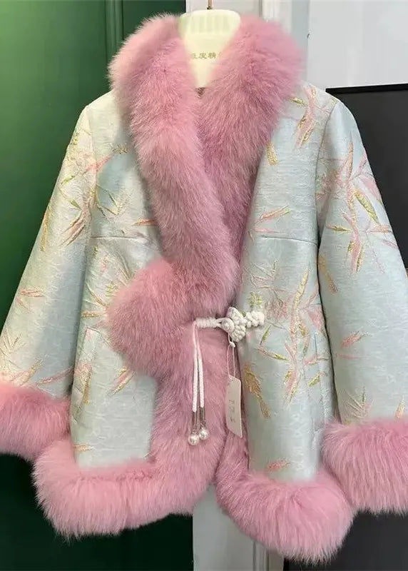 A light blue-green embroidered jacket with pink fur trim, displayed on a hanger against a dark green wall.