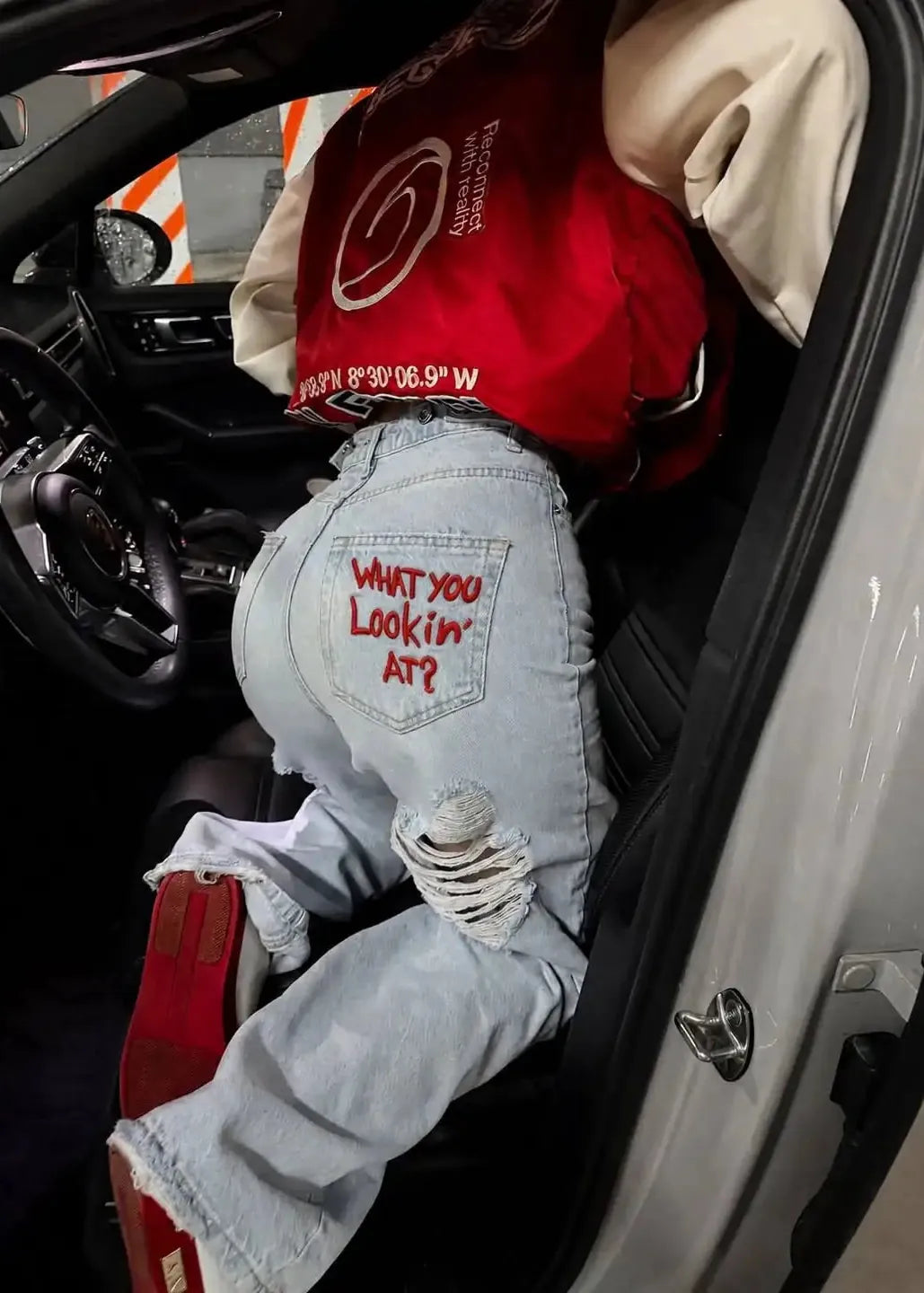 Person wearing a red shirt and light blue jeans with text inside a car.
