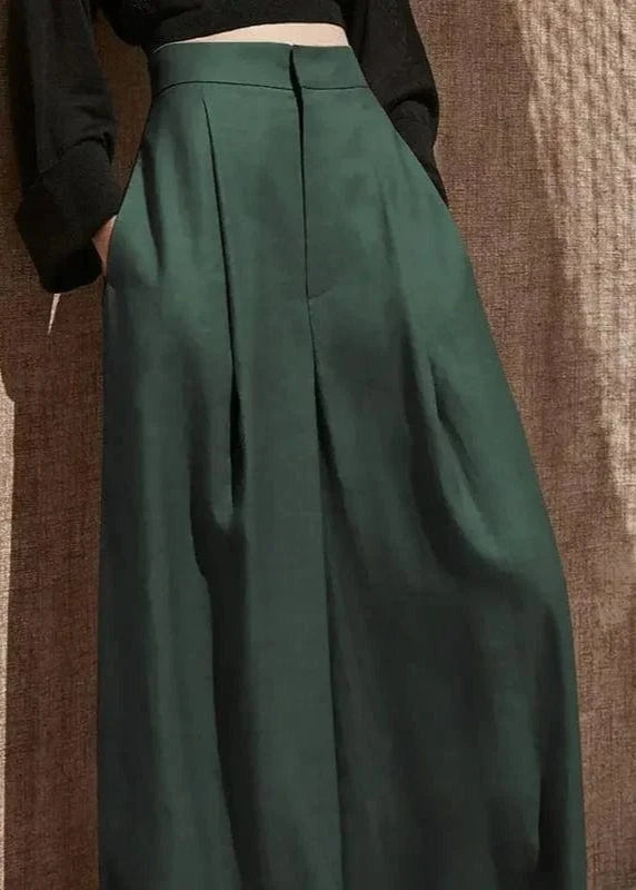 Green pleated skirt worn by a person against a textured brown wall.