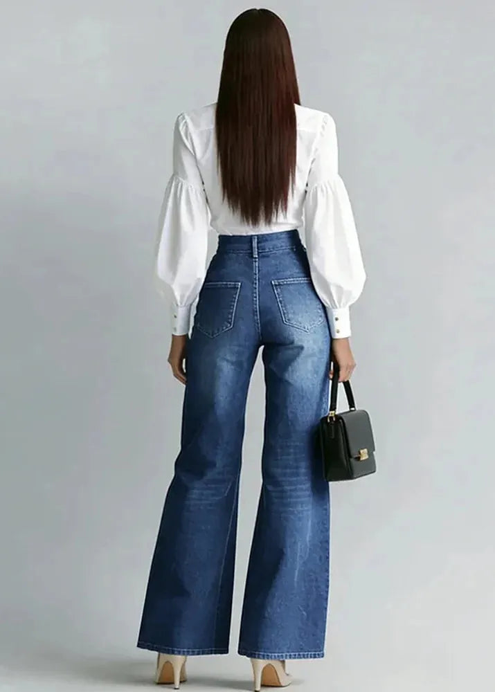 Woman wearing blue jeans and a white blouse, holding a black handbag on a gray background