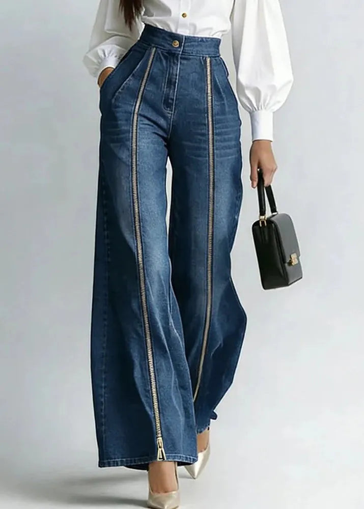 Person wearing blue jeans with zippers, holding a black handbag on a plain background