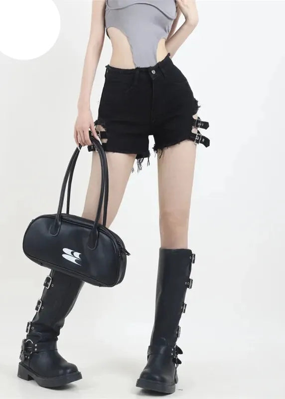 Person wearing black high-waisted shorts and black knee-high boots holding a black handbag on a white background.