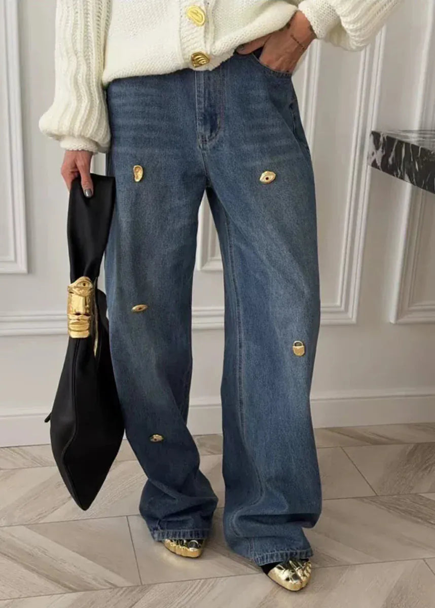 Person wearing blue jeans with gold buttons in a room with white walls and wooden floor.