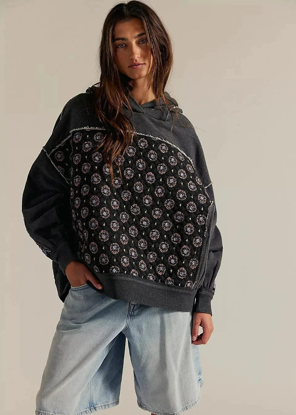 Woman wearing a black patterned hoodie and denim shorts on a plain background