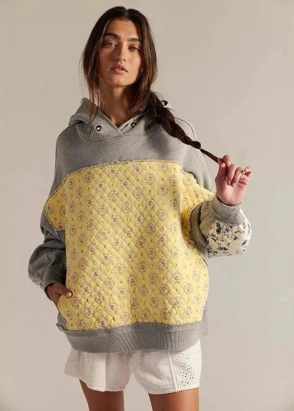 Woman wearing a gray and yellow quilted hoodie against a plain background