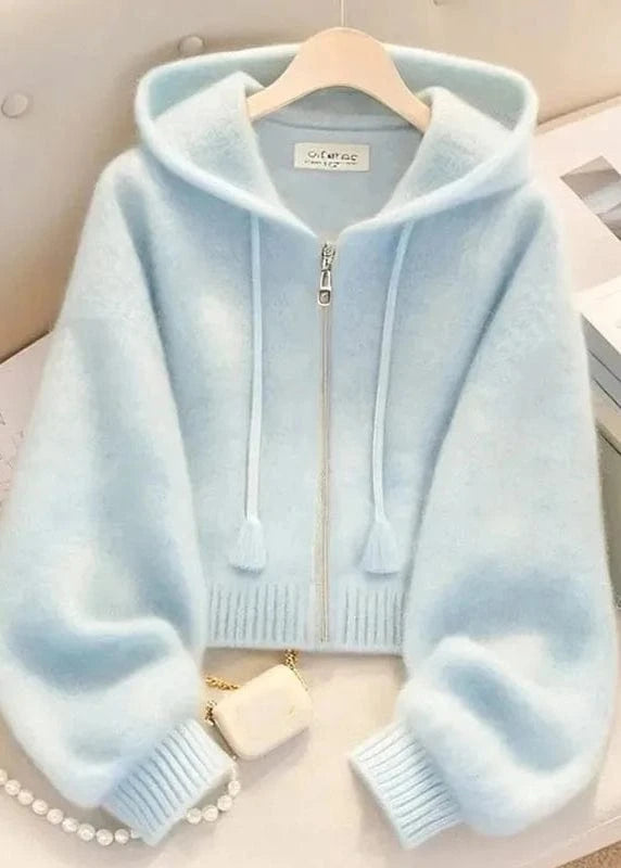 Light blue hoodie on a hanger with a pearl necklace and heart-shaped object in the background.