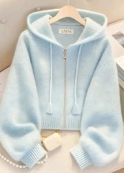 Light blue hoodie on a hanger with a pearl necklace and heart-shaped object in the background.