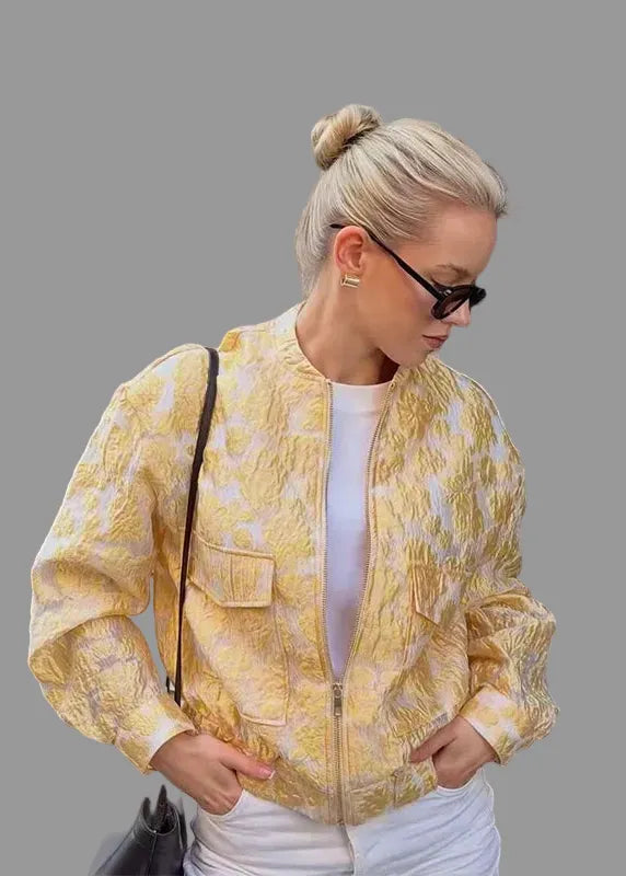 Woman wearing a yellow patterned jacket in front of a black gate.