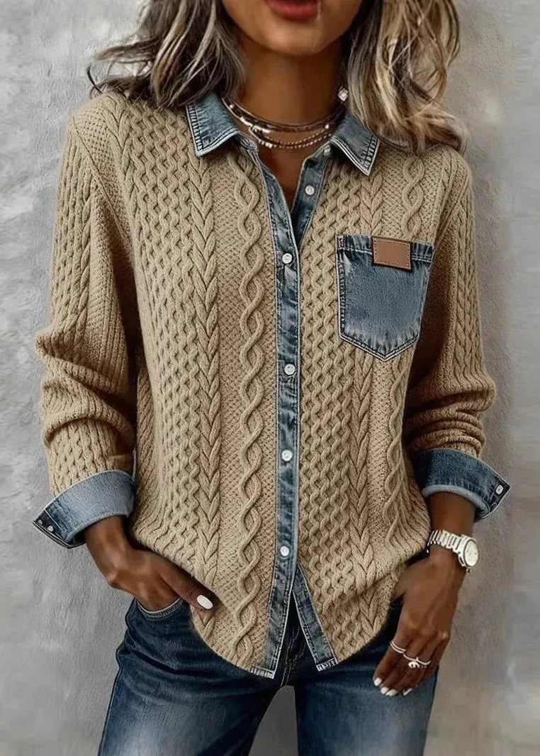 Person wearing a beige cable knit sweater over a denim shirt with rolled-up sleeves against a gray background.