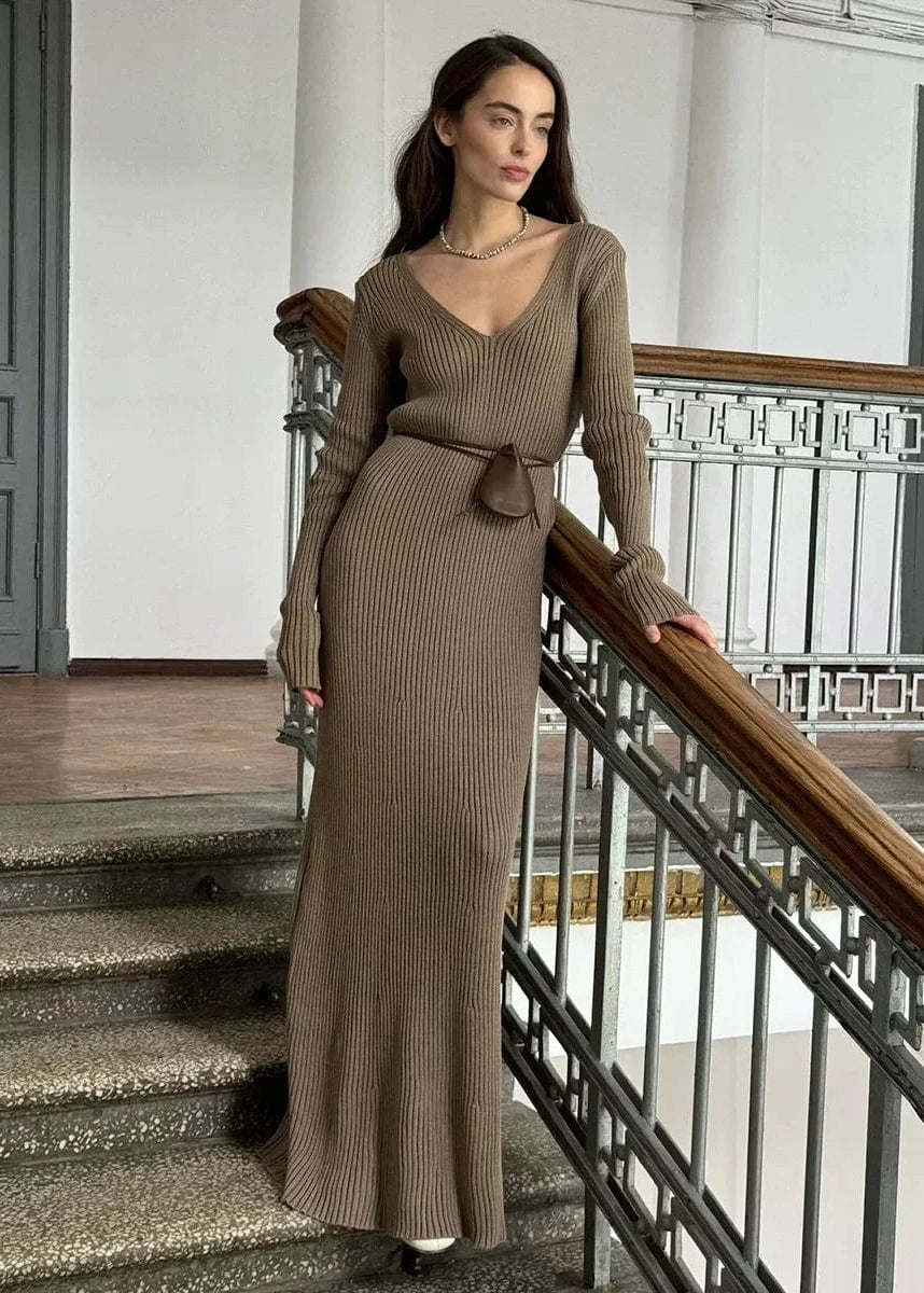 Woman in a long brown dress standing on a staircase.