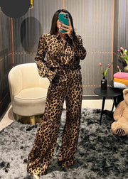 Person wearing a leopard print outfit taking a mirror selfie in a room with a chair, table, and teddy bear.