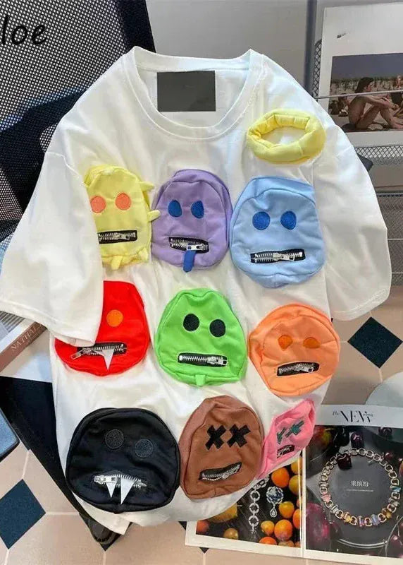 White t-shirt with colorful emoji-like face designs on a magazine