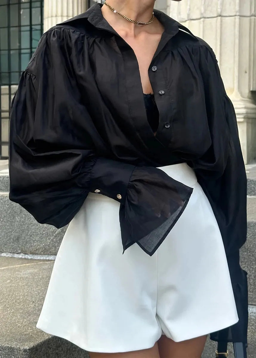 Person wearing a black oversized shirt and white shorts outdoors.