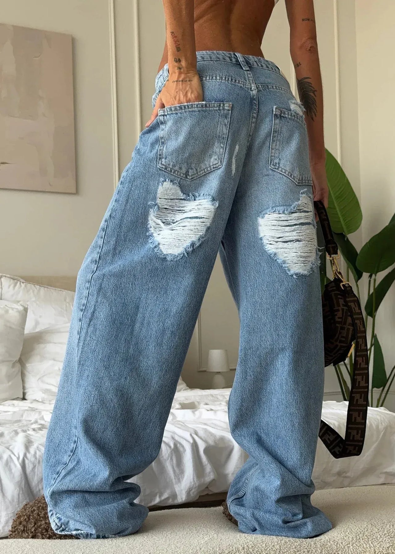 Person wearing ripped blue jeans in a bedroom setting