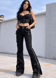 A woman modeling a black gothic-style outfit consisting of a lace-trimmed corset top and black flared jeans with side hardware, standing outdoors against a light gray wall.