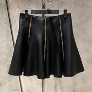 Black leather skirt with gold zipper on a hanger against a concrete wall.
