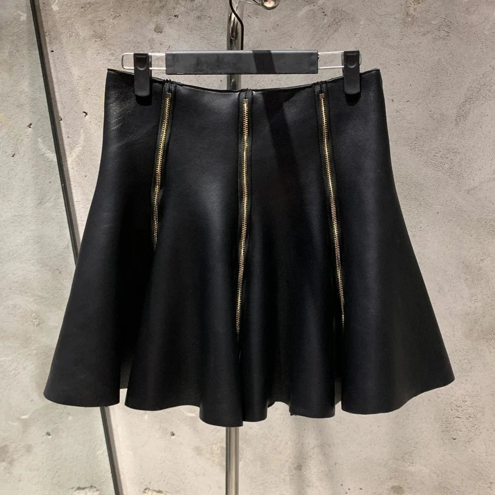 Black leather skirt with gold zipper on a hanger against a concrete wall.
