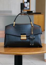 Black crocodile-patterned handbag with gold accents on a wooden table.