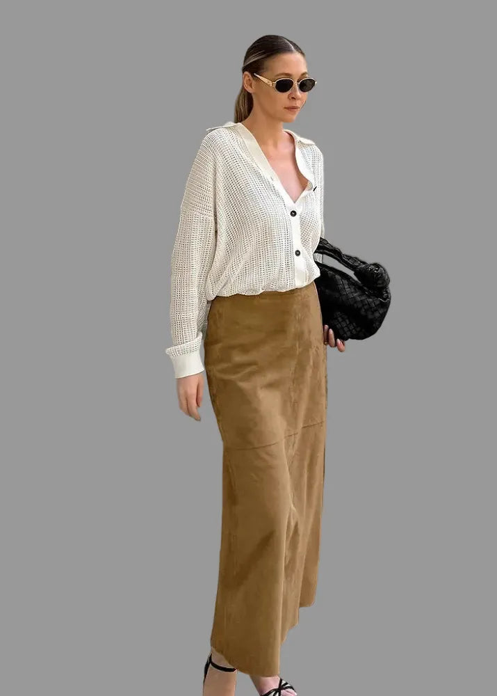 A woman stands outdoors in front of a building entrance wearing a white ribbed knit button-front cardigan, a brown midi skirt, sunglasses, and carrying a black textured handbag. The Singreini brand logo is visible in the top left corner.