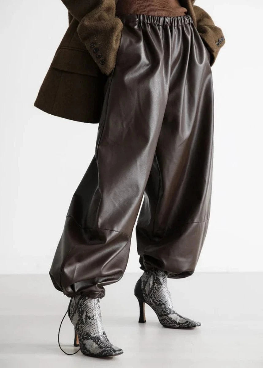 Brown leather pants worn with a brown coat on a white background