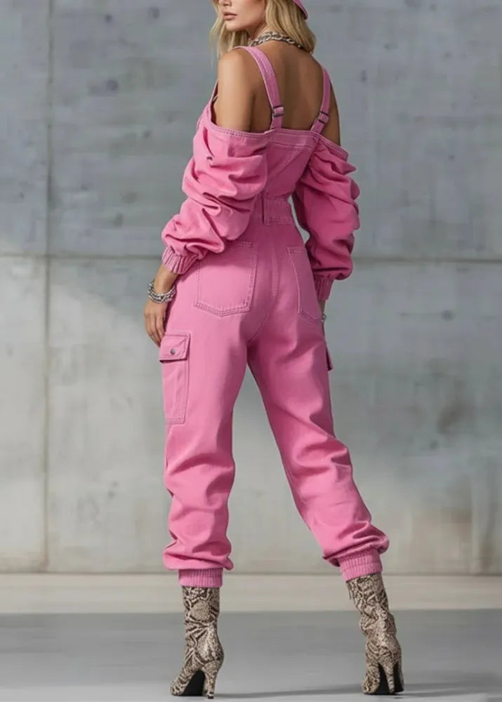 Person wearing a pink jumpsuit with cut-out shoulders against a concrete wall.