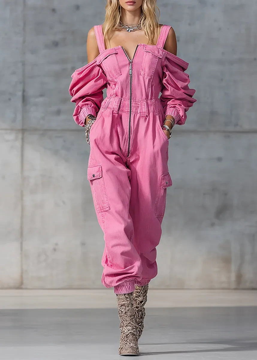 Person wearing a pink jumpsuit with ruffled sleeves against a gray concrete wall.