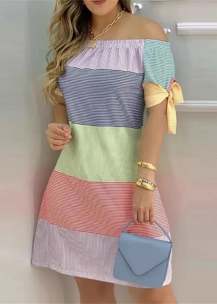 Woman wearing a colorful off-shoulder dress holding a blue handbag.