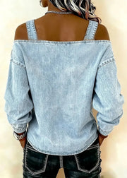 Person wearing a light blue denim shirt with rolled-up sleeves on a beige background