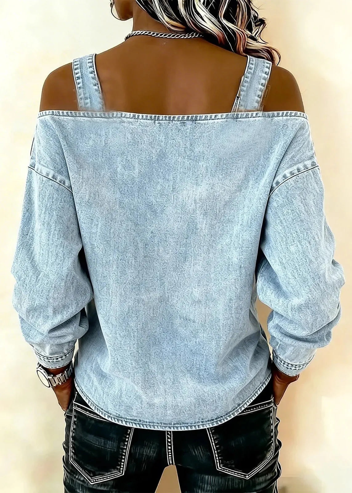 Person wearing a light blue denim shirt with rolled-up sleeves on a beige background