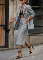 Woman in a stylish outfit with a gray blazer and skirt walking outdoors.