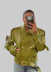 A woman takes a mirror selfie in a clothing store wearing a structured olive green faux leather jacket with gold-tone buttons and a matching belt, paired with light blue jeans.