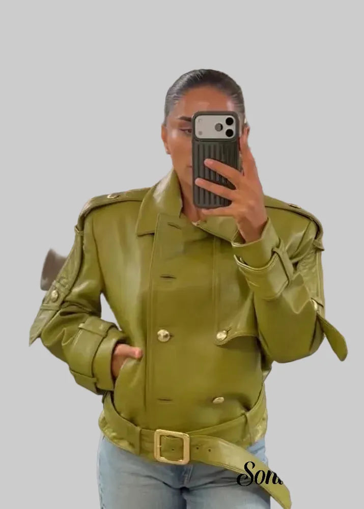 A woman takes a mirror selfie in a clothing store wearing a structured olive green faux leather jacket with gold-tone buttons and a matching belt, paired with light blue jeans.