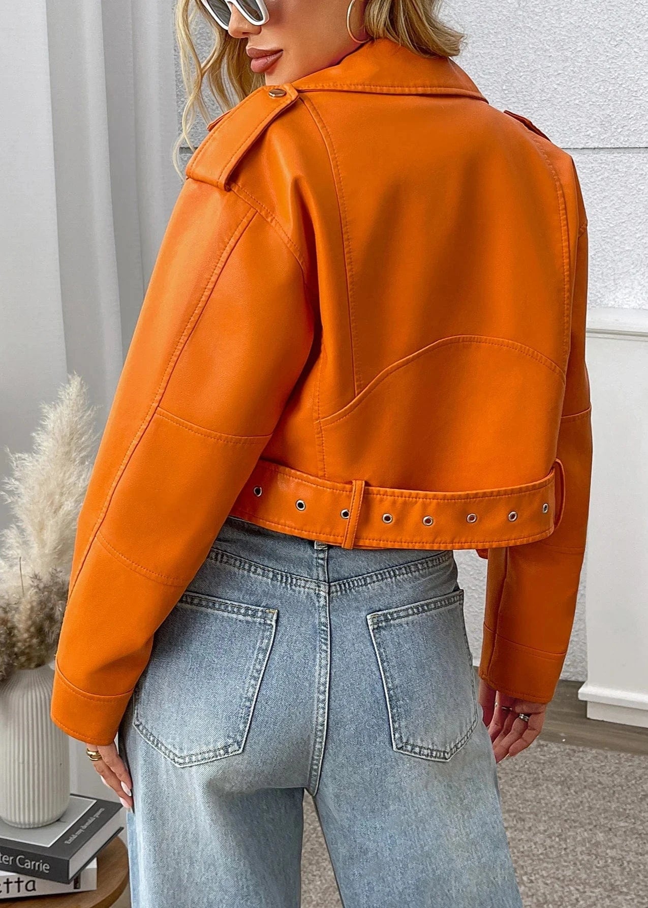 Person wearing an orange leather jacket and light blue jeans indoors.
