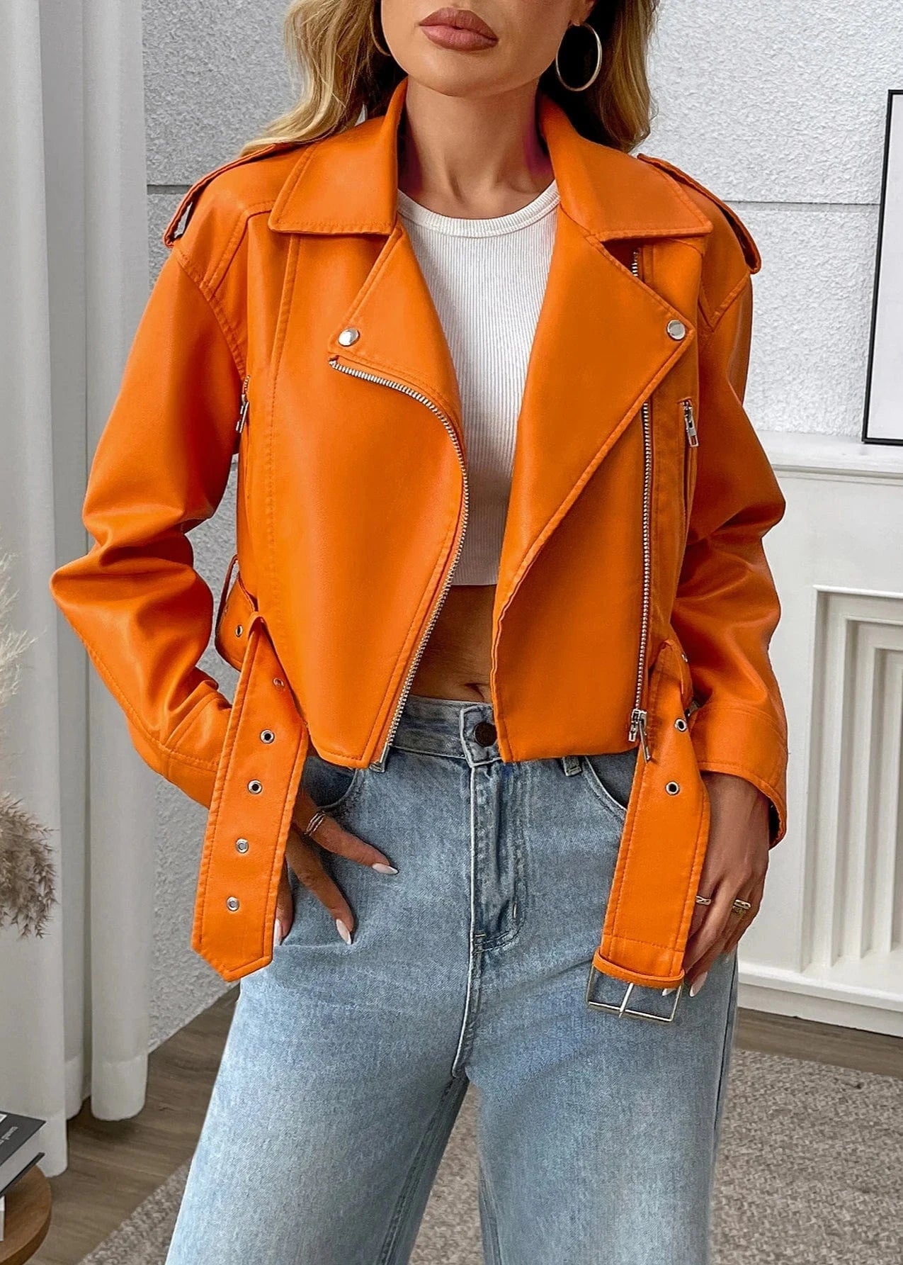 Person wearing an orange leather jacket and blue jeans indoors.