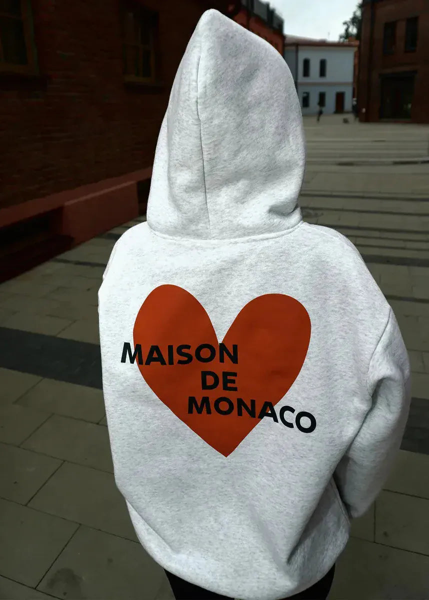 Gray hoodie with a red heart and 'MAISON DE MONACO' text on the back, worn outdoors.