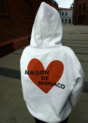 Gray hoodie with a red heart and 'MAISON DE MONACO' text on the back, worn outdoors.