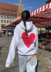 Person wearing a hoodie with a red heart and text in an outdoor market setting