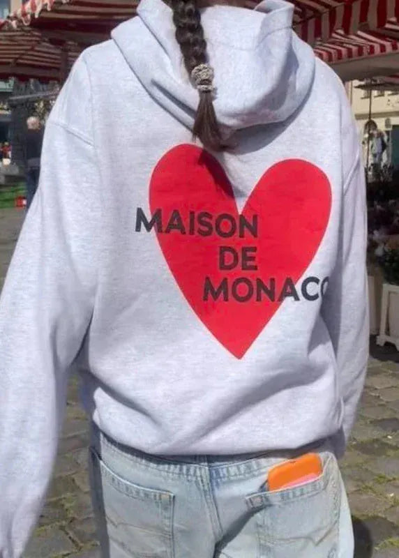Person wearing a hoodie with a red heart and 'MAISON DE MONACO' text in an outdoor setting.