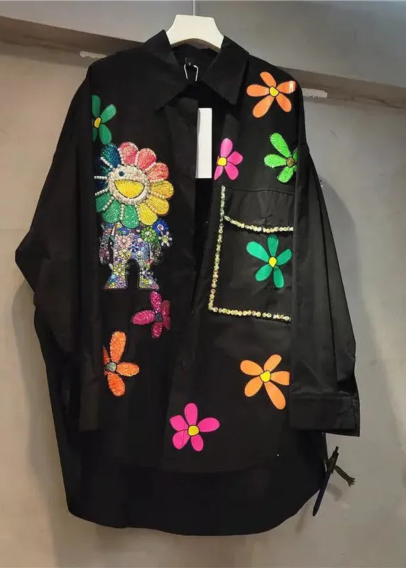 Black shirt with colorful floral and animal designs on a hanger against a neutral background