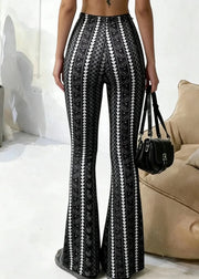 Person wearing black and white patterned pants holding a black handbag indoors.