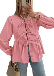 Person wearing a pink jacket with a tie waist, holding a beige handbag.