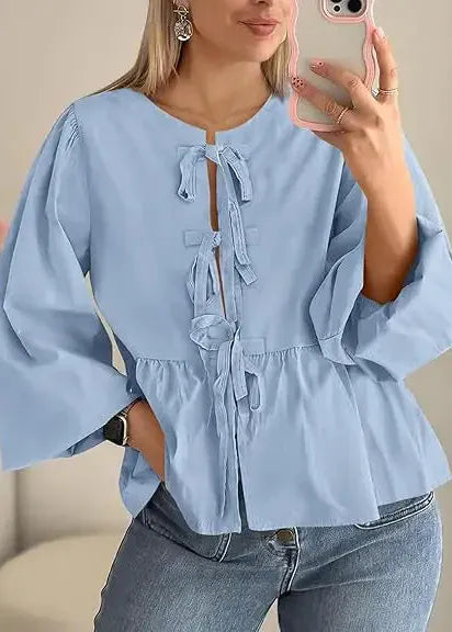Woman wearing a light blue blouse with ruffled details and jeans, taking a mirror selfie.