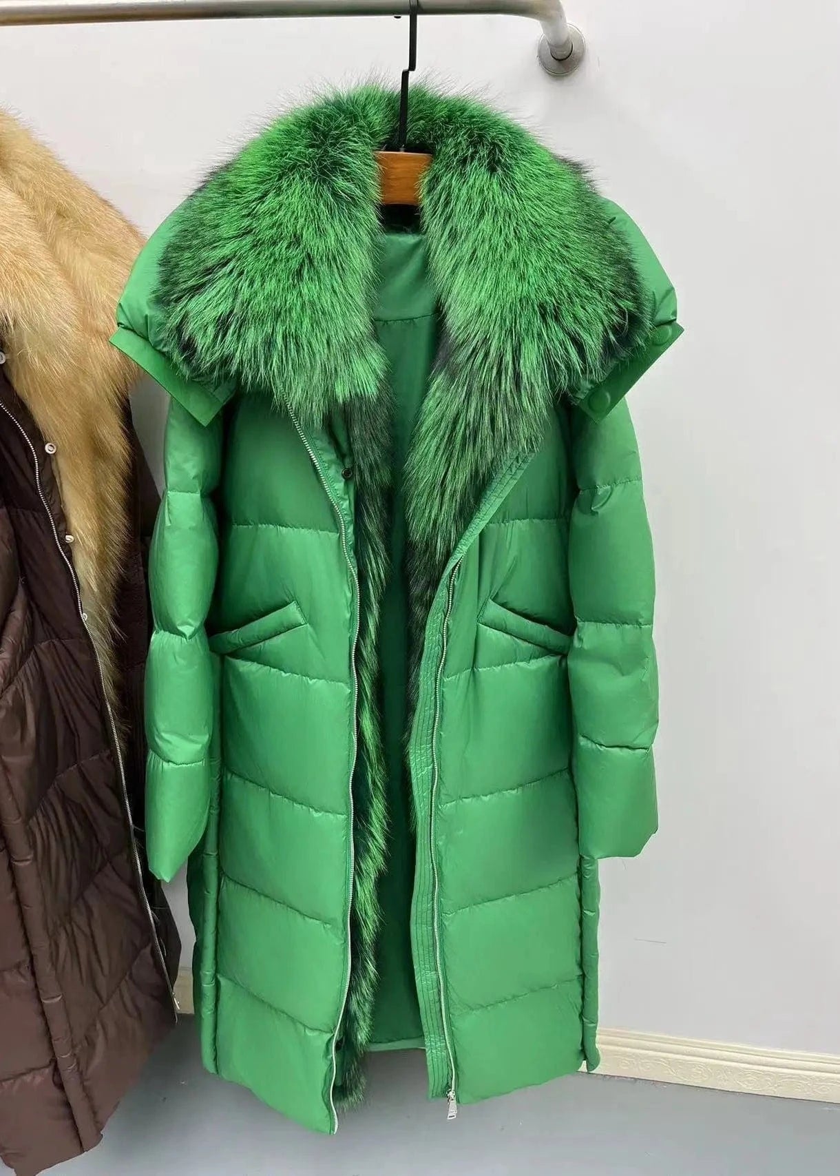 Green puffer coat with fur collar on a hanger against a plain background