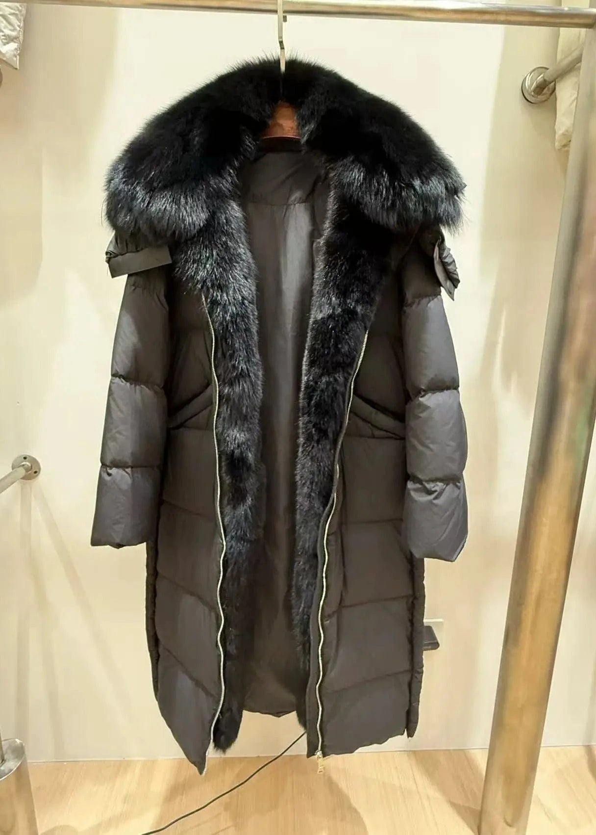 Gray puffer coat with fur-lined hood on a hanger against a neutral background