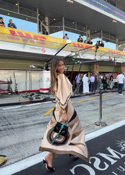 Woman in a stylish outfit with a large umbrella at a race track, with 'DHL' and 'Maserati' branding visible.