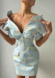 A woman wearing a light blue off-the-shoulder bodycon mini dress with a beige and green floral print, featuring a deep V-neckline with decorative buttons and flap pockets.